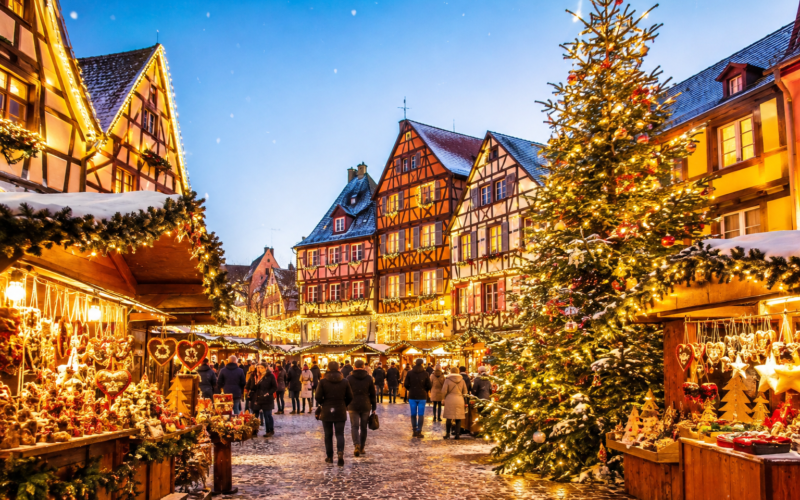 Chalets décorés et grand sapin illuminé dans un village alsacien aux maisons à colombages.