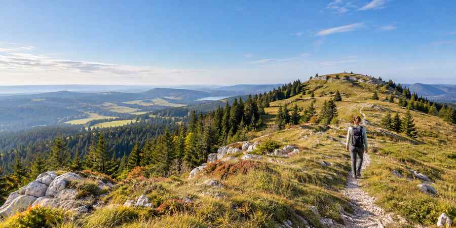 Randonneuse sur un sentier du Crêt Pela au-dessus des forêts du Jura